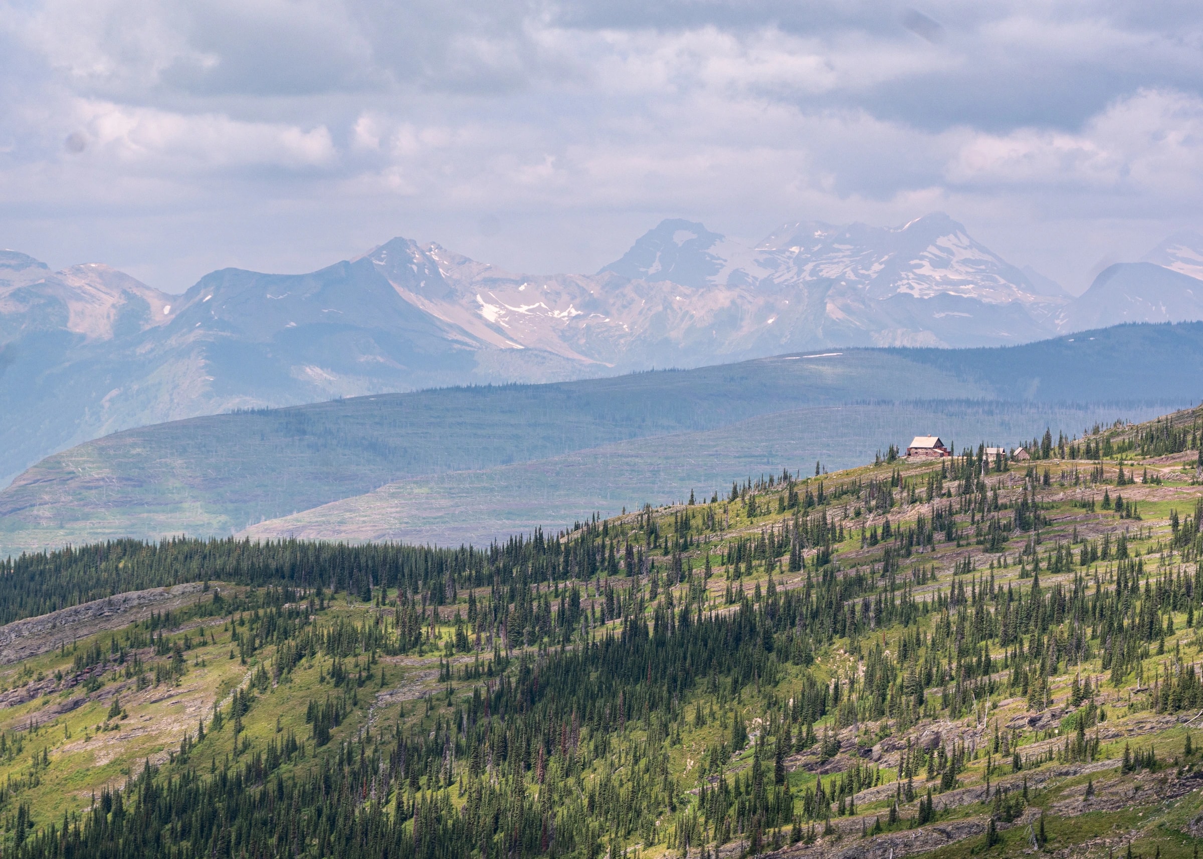 Mountain panorama in Glacier National Park, forested ridge and small cabin in mid-ground.