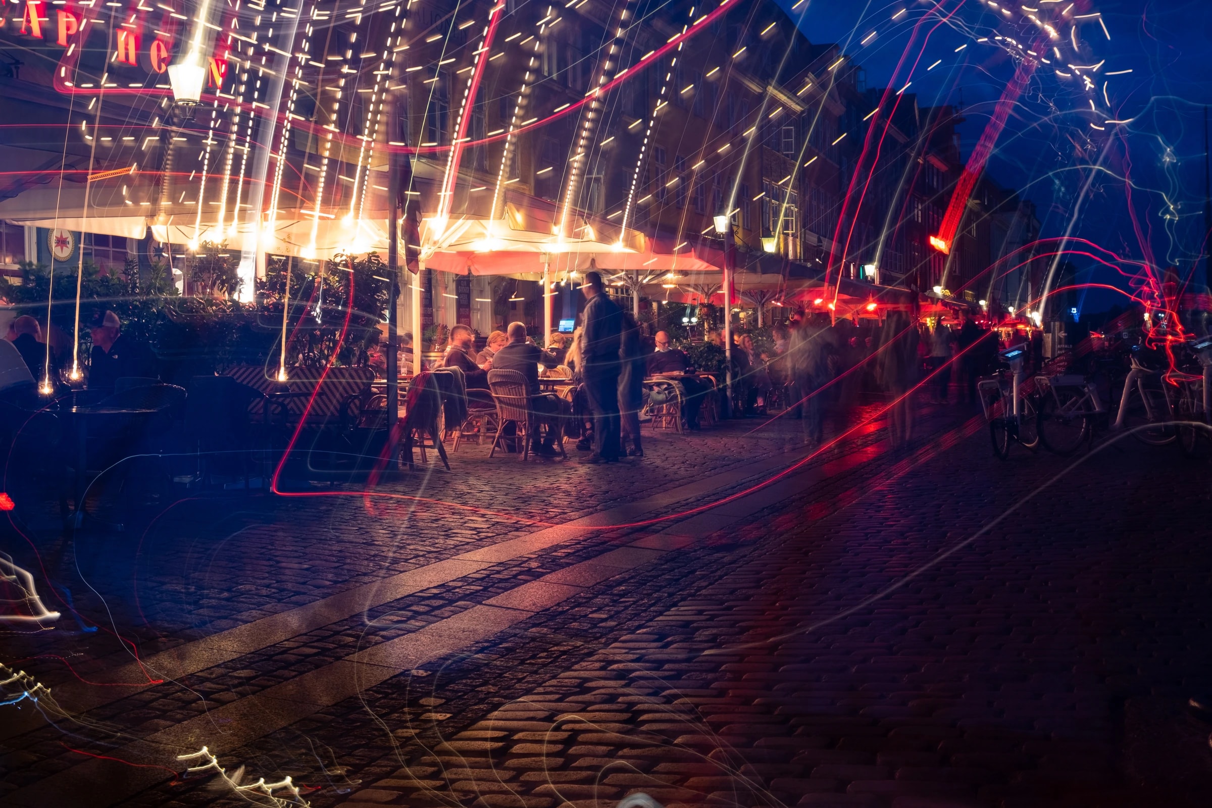 Long-exposure shot of Nyhavn, Copenhagen, red and white light trails overlaying outdoor cafe diners.
